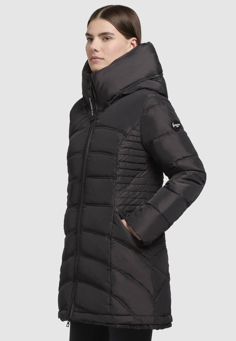 Doudoune noire avec un col haut et ajustable, motif matelassé, deux poches latérales et une finition lisse et brillante. Fermeture frontale zippée.