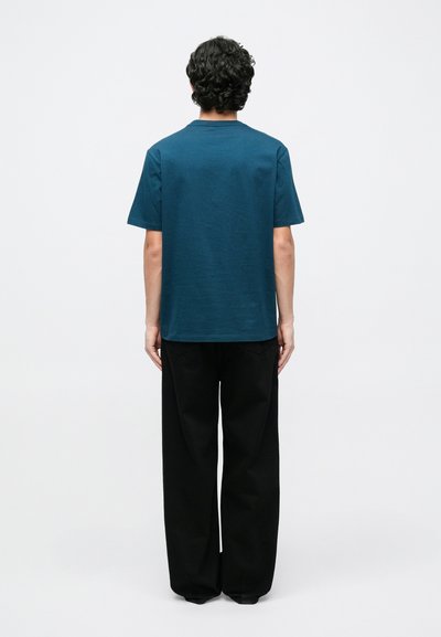 Pūderkrāsas zils T-krekls no mīksta auduma ar klasisku apaļu apkakli un īsām piedurknēm, kopā ar vaļīgām tumšām biksēm.