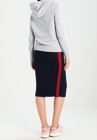 Sudadera con capucha gris combinada con una falda de rodilla azul marino que presenta rayas laterales rojas. Llevada con zapatillas de deporte rosa claro.