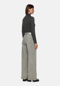 Grauer langärmliger Rollkragenpullover mit tailliertem Design, kombiniert mit hochgeschnittenen, weit geschnittenen hellgrauen Jeans und schwarzen klobigen Stiefeln.