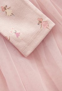 Rosa ribbat tyg med tryckta illustrationer av dansande möss i klänningar, placerad på hopvikt rosa tylle-material.