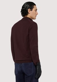 Burgundský pletený svetr s límečkem, slim fit, a žebrovaným lemem; kombinovaný s tmavě modrými semišovými kalhotami a černými koženými rukavicemi.