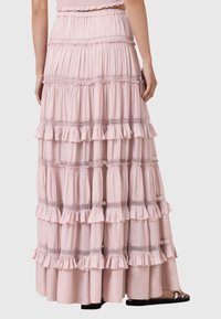Falda maxi en capas de tela rosa suave, con capas con volantes y costuras decorativas entre las capas. Ajuste casual con un diseño fluido.