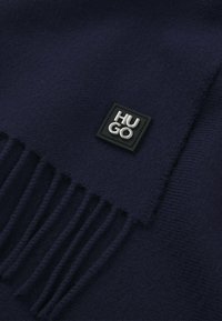 Sciarpa in lana navy con finitura testurizzata, bordi frangiati e un'etichetta quadrata in gomma nera con la scritta "HUGO."