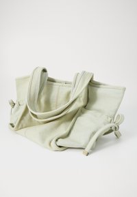 Borsa tote in tela verde chiaro, dal design morbido, con due lunghe maniglie, lacci laterali e dettagli di cucitura a contrasto. Texture morbida, aspetto casual.