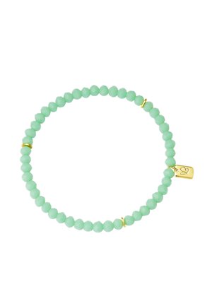 Bracelet extensible avec petites perles rondes vert clair et trois anneaux intercalaires en or, avec une petite étiquette en or ornée d'un symbole de cœur.