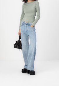 Top a maniche lunghe verde chiaro, jeans azzurri a vita alta e a gamba larga, borsa nera con motivo, scarpe con plateau nere e spesse.