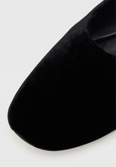 Chaussure plate en velours noir avec une pointe en amande, texture lisse et design bas. L'intérieur est doublé de matériau noir.