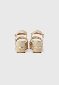 Sandali platform beige con suola in jute intrecciato, cinturino alla caviglia singolo e dettagli metallici. Texture liscia e design del tacco arrotondato.