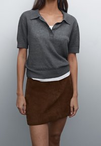 Grijze korte mouwen polo trui met een kraag en drie knopen, gecombineerd met een bruin suède minirok, met een soepele textuur en een aansluitend ontwerp.