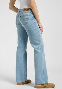 Jeans acampanados en un azul claro con un parche de cuero marrón de la marca Lee en la cintura, que cuentan con cinco bolsillos y detalles de costura visibles.