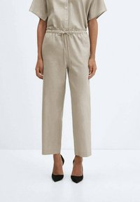 Pantalon beige ample avec taille élastique et cordon de serrage. Fabriqué en tissu lisse et léger. Devant plat, jambes droites.