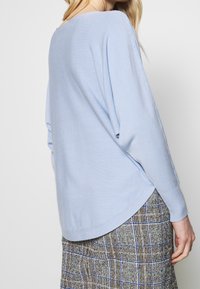 Ljusblå stickad tröja med avslappnad passform, långa ärmar och sidospjäll, kombinerad med en rutig texturerad kjol med blå och bruna ränder.