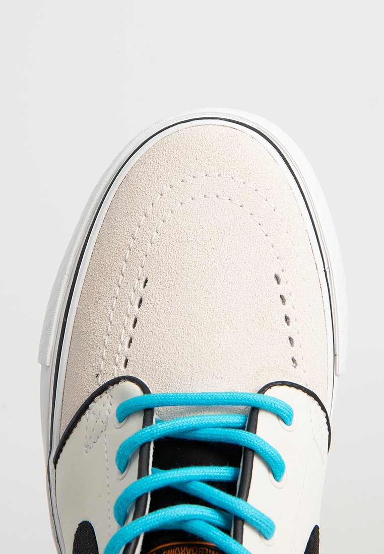 Zapatillas de ante y textil con una parte superior beige, acentos negros y cordones turquesa. Presentan una suela de goma blanca y detalles de diseño perforados.