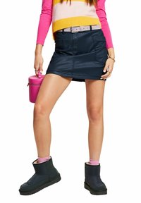 Czarna spódnica z imitacji skóry z przednimi kieszeniami, zestawiona z różowym swetrem i różową torbą typu bucket. Modelka ma na sobie czarne botki za kostkę z różowymi skarpetkami.