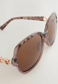 Überdimensionale Sonnenbrille mit einem durchscheinenden braunen Schildpatt-Rahmen, braunen Gläsern und roségoldenen Beschlägen. Verfügt über detaillierte Kettenakzente an den Bügeln.