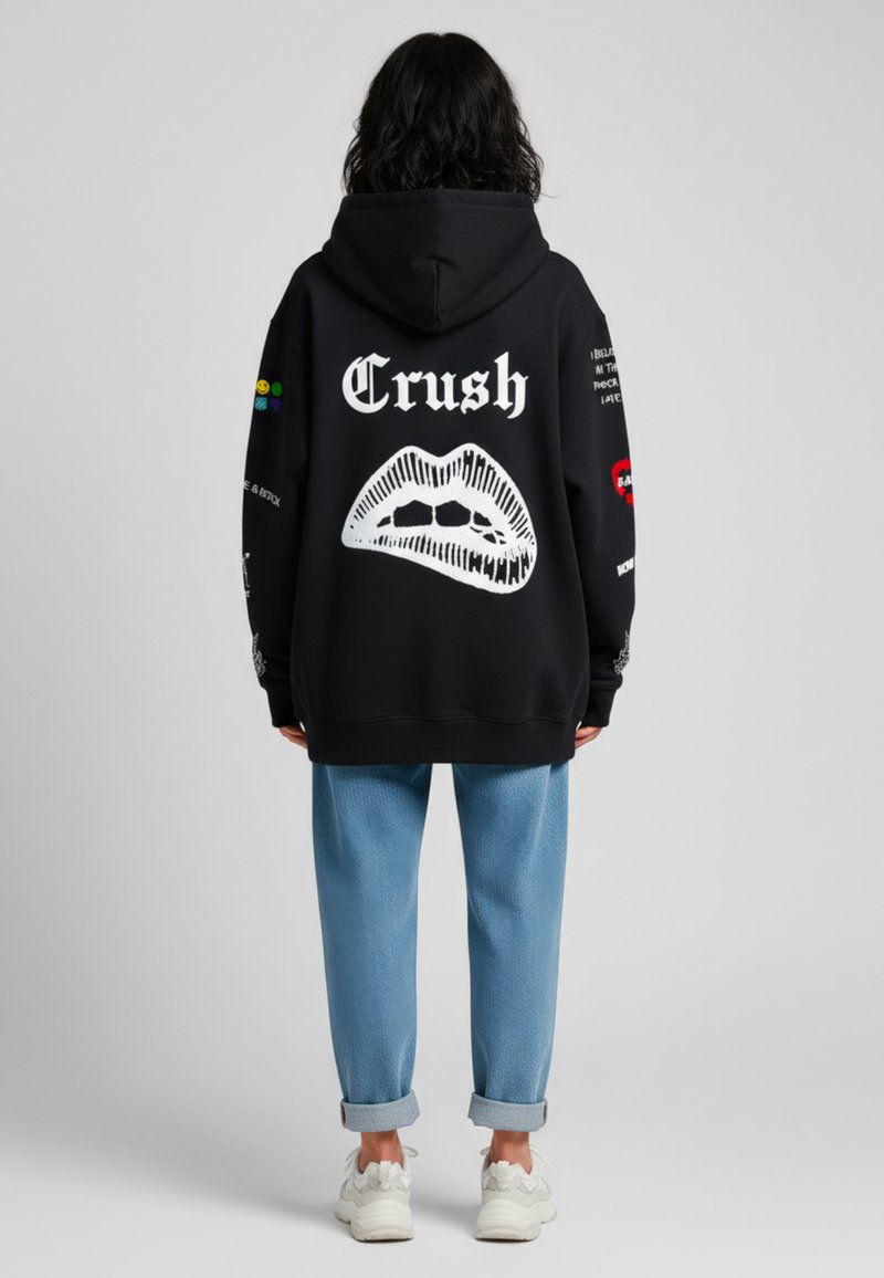 Felpa nera con grafica di labbra bianche e testo "Crush" sulla schiena. Abbinata a pantaloni blu chiaro con risvolti e scarpe da ginnastica bianche.