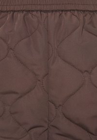 Tissu matelassé marron avec motif de coutures ondulées et ceinture élastique rassemblée en haut.