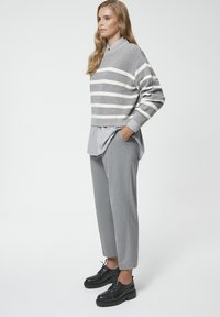 Szary sweter w paski z okrągłym dekoltem nałożony na szary podkoszulek, w komplecie z szarymi spodniami i czarnymi wiązanymi butami.