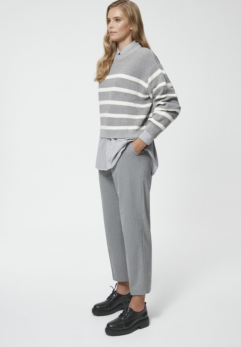 Szary sweter w paski z okrągłym dekoltem nałożony na szary podkoszulek, w komplecie z szarymi spodniami i czarnymi wiązanymi butami.