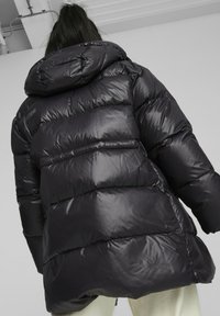 Černá péřová bunda s lesklým povrchem, v oversized stylu, prošívaný design a viditelné švy. Má delší zadní délku pro zvýšenou ochranu.