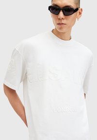 White cotton t-shirt featuring raised "ALLSAINTS LONDON" text. Crew neck, short sleeves, relaxed fit, smooth texture. Simple design.