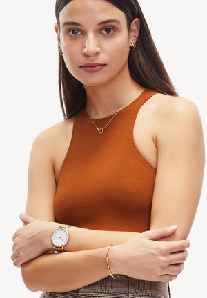 Haut sans manches couleur rouille en tissu texturé, associé à une montre en or et un bracelet, présentant un design simple et élégant.