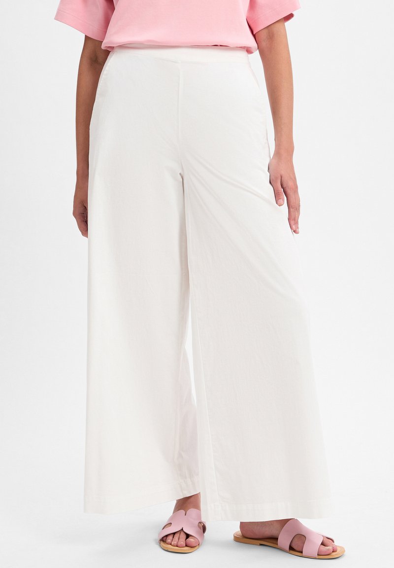 Weite, weiße Baumwollhosen mit glatter Textur und versteckten Seitentaschen. Kombiniert mit pinken Rutschschuhsandalen für einen lässigen Look.