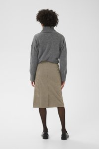 Suéter gris de punto con cuello alto; debajo, una falda a la rodilla con patrón pata de gallo. Medias negras y zapatos negros gruesos completan el conjunto.