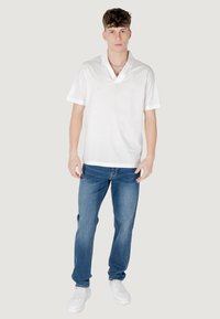 Polo bianco a maniche corte con scollatura a V, abbinato a jeans in denim blu e sneakers bianche, creando un look informale.