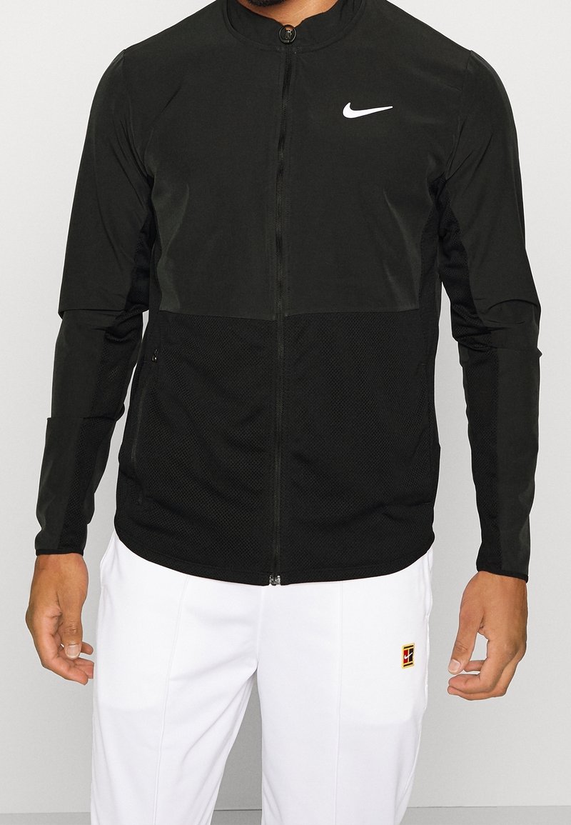 Black Nike jacket featuring a zip front, mesh panels, long sleeves, and a curved hem; complemented by a white logo on the chest.