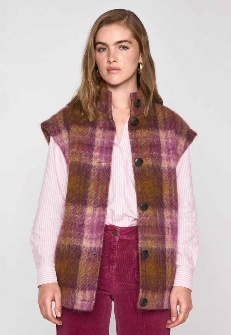 Gilet en laine à carreaux roses, violets et bruns. Manches courtes, col montant et boutons noirs sur le devant. Fini texturé.