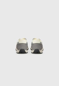 Baskets de sport grises et crème avec une tige en daim et en maille, forme arrondie et semelle extérieure en caoutchouc noir texturé pour une meilleure adhérence.