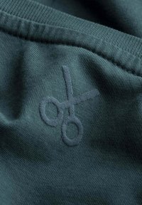 Donkergroene stof met een tone-on-tone geborduurd schaarontwerp, dat een zachte textuur en een gladde afwerking benadrukt.