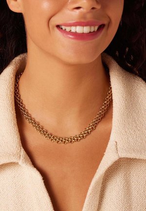 Collier en or avec plusieurs maillons entrelacés, design superposé, texture lisse, porté sur un vêtement texturé de couleur claire.
