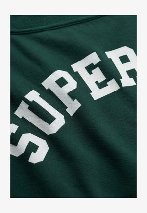 Zielona tkanina z pogrubionymi białymi wielkimi literami układającymi się w słowo "SUPER" w zakrzywionym układzie.