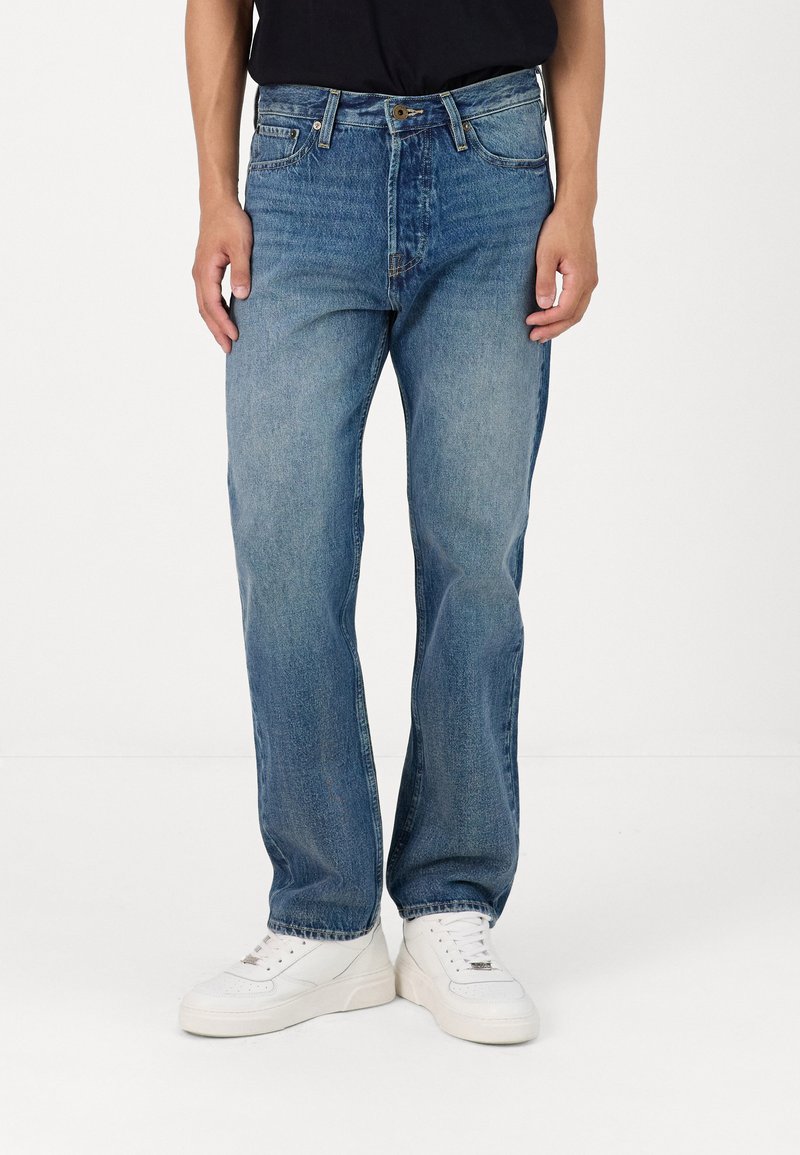 Light blue straight-leg jeans with a faded wash, five pockets, and metal button closure, paired with white sneakers.