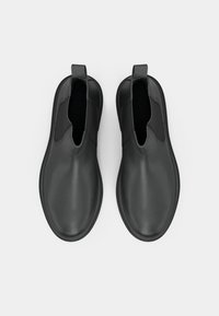 Chaussures noires à enfiler avec une finition lisse et mate, des panneaux latéraux élastiques et une languette arrière pour un enfilage facile. Semelle plate et texturée.