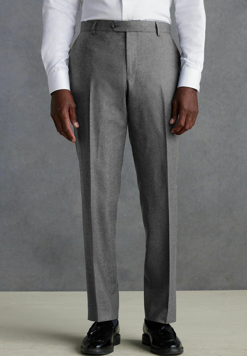 Pantalones grises ajustados en una mezcla de lana texturizada, con un frente plano, dos bolsillos laterales y un corte entallado, combinados con zapatos negros.