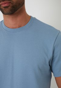 Světle modré tričko s krátkým rukávem vyrobené z texturované látky, s designem kulatého výstřihu a bezšvovou konstrukcí ramen.