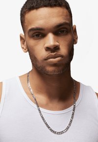 Silver chain necklace worn over a white ribbed tank top. The necklace features a classic curb link design with a polished texture.