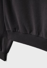 Gros plan sur le bord de manchette et la ceinture d'un sweat-shirt noir avec une texture en tricot côtelé sur fond blanc.