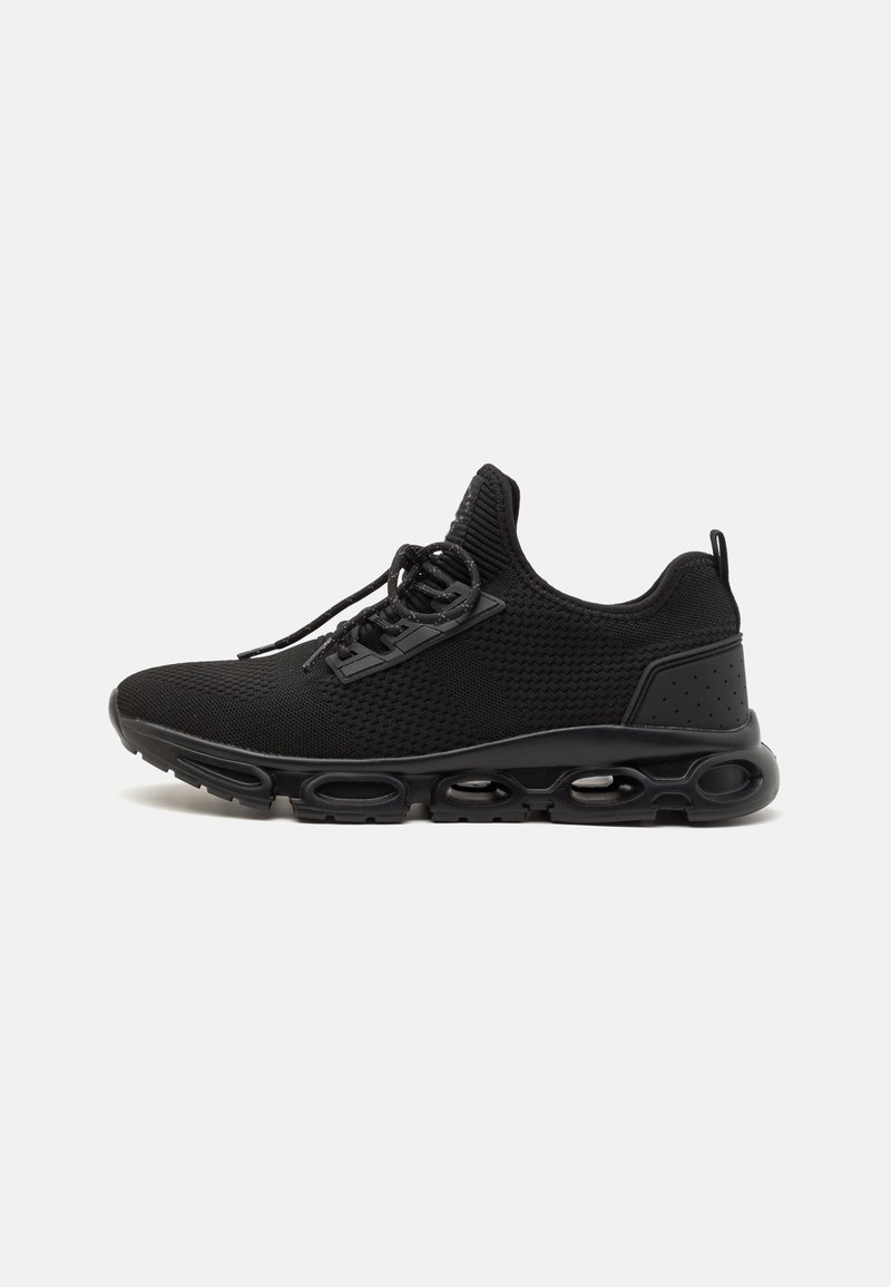 Zapatilla deportiva de malla negra con un upper texturizado, cordones elásticos y una suela acolchada con recortes circulares para ventilación.