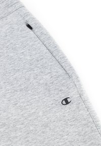 Pantaloni sportivi grigi con tasca con zip e un piccolo logo nero sulla parte inferiore della gamba, realizzati in un tessuto morbido e texturizzato.