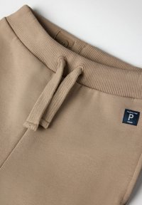 Beige sweatpants med ribbet talje, justerbar snor og et mærke med "P" og "SWEDEN" i en kontrasterende marineblå farve.