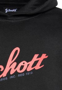 Felpa nera con cappuccio caratterizzata da un logo rosa prominente che recita "Schott" con un testo più piccolo sottostante. Il materiale sembra morbido con una texture liscia.