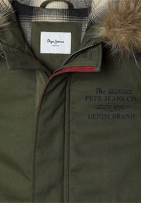 Zaļš parka ar mākslīgās kažokādas apdari, ar pārbaudītu oderi, rāvējslēdzēju, izšūtu tekstu un sarkaniem akcentiem. Klāt ir Pepe Jeans zīmols.