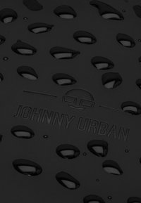 Superficie negra y texturizada con recortes ovalados y el logo "JOHNNY URBAN" en relieve, diseñada para el drenaje y el control de la humedad.