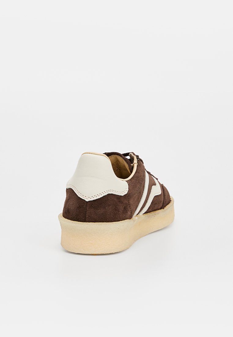 Baskets en suede marron avec un accent de talon en cuir blanc, tige texturée, rayures blanches contrastantes et semelle en caoutchouc beige.