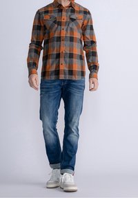 Pomarańczowo-szara koszula flanelowa w kratę z długimi rękawami, dwoma kieszeniami na piersi, zapinana na guziki, noszona z niebieskimi dżinsami i białymi tenisówkami.